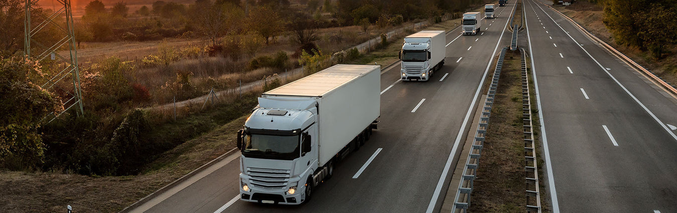 four large white lorries travelling down a main road in single file 